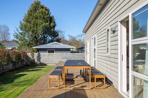 Eine Holzterrasse mit Tisch und Stühlen, ein Haus mit Metalldach und ein großer Baum im Hintergrund.