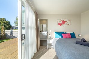 Ein Schlafzimmer mit einem Bett, einem Nachttisch, einem Spiegel und Blick ins Freie.