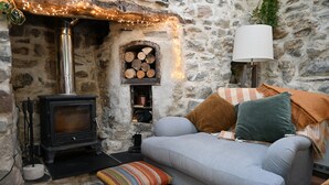 Una habitación acogedora con pared de piedra, chimenea, sofá y lámpara.