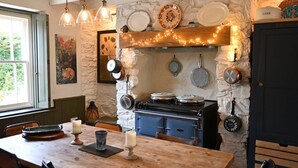 Una cocina acogedora con pared de piedra, mesa de madera y ollas colgantes.