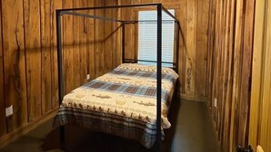 Um quarto com painéis de madeira, uma cama com dossel, um ventilador de teto e uma janela com persianas.
