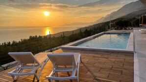 A poolside area with lounge chairs and a view of the sea and mountains during sunset. - Stunning home in Podgora (Podgora)