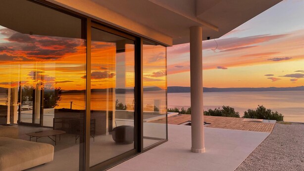 A modern interior with large glass doors leading to a terrace with a sunset view. - Stunning home in Podgora (Podgora)