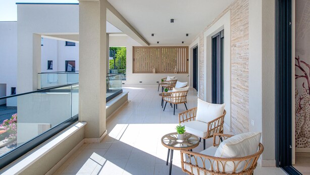 A balcony with wicker furniture and a glass table, overlooking a modern building and a staircase.