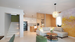 A modern living room with a sofa, ottoman, and coffee table, a staircase, and a kitchen in the background.