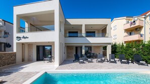 A modern two-story building with a pool area, outdoor seating, and a visible name sign.