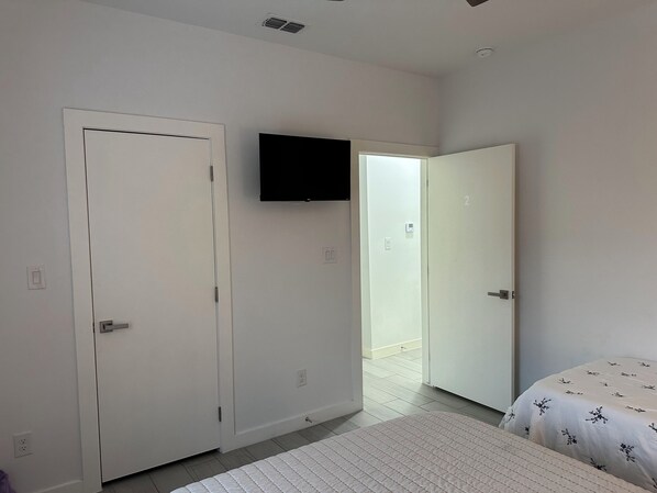 A bedroom with a bed, a TV mounted on the wall, and two doors leading to other rooms.