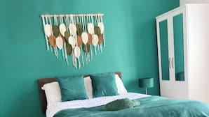 Un dormitorio con cama, paredes color verde azulado, un tapiz de macramé y un armario.