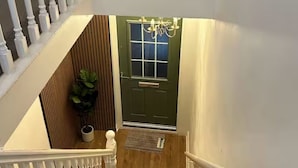 Una escalera con barandillas blancas, una puerta verde con un ventanal y un candelabro.