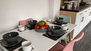 Una mesa de comedor dispuesta con cuencos negros, tazas blancas y un frutero.