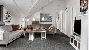 Een moderne woonkamer met een grijze bank, een ronde salontafel en een televisie op een witte kast.