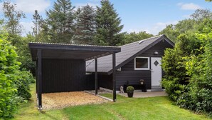 Een klein, donker houten huis met een overdekte veranda en een kleine tuin.