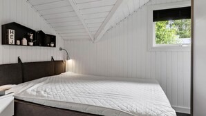 Een slaapkamer met een bed, nachtkastje, bureau, lamp en raam met uitzicht op groen.