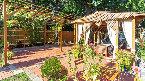 Un jardin agrémenté d’une pergola en bois, d’un kiosque et d’un espace patio avec une table et des chaises.