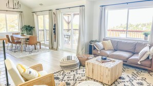 A spacious living room with a large window, a wooden coffee table, a sofa, and a dining area with chairs and a table.