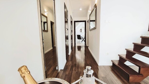 Un couloir moderne avec un plancher en bois, un escalier et une bouteille de champagne posée sur un chariot.