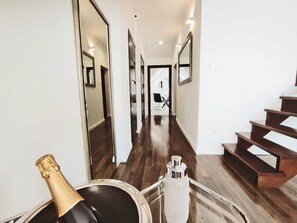 A modern hallway with wooden flooring, a staircase, and a champagne bottle on a cart.