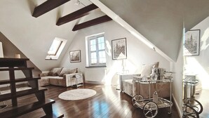 Un loft spacieux avec un plafond haut, des poutres en bois, un coin salon confortable avec un canapé et des fauteuils, un tapis rond et une table accessible aux personnes en fauteuil roulant, dotée d’un plateau.