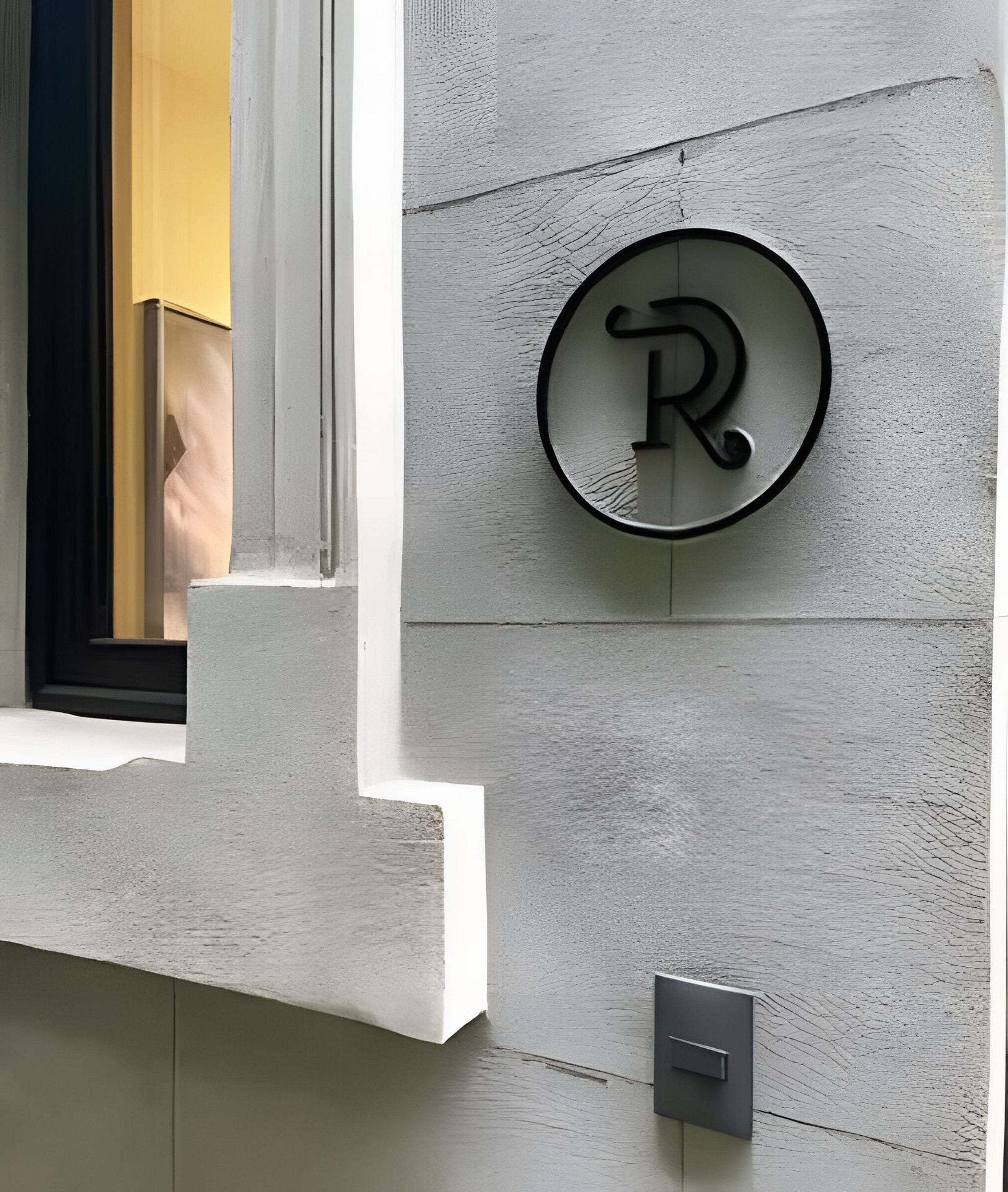 Une façade d’immeuble ornée d’une enseigne circulaire sur laquelle figure la lettre « R » en majuscules.