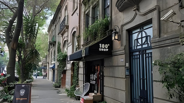 Una calle estrecha con edificios históricos, una tienda llamada "180° SHOP" con toldo negro, y una antena parabólica en la acera.