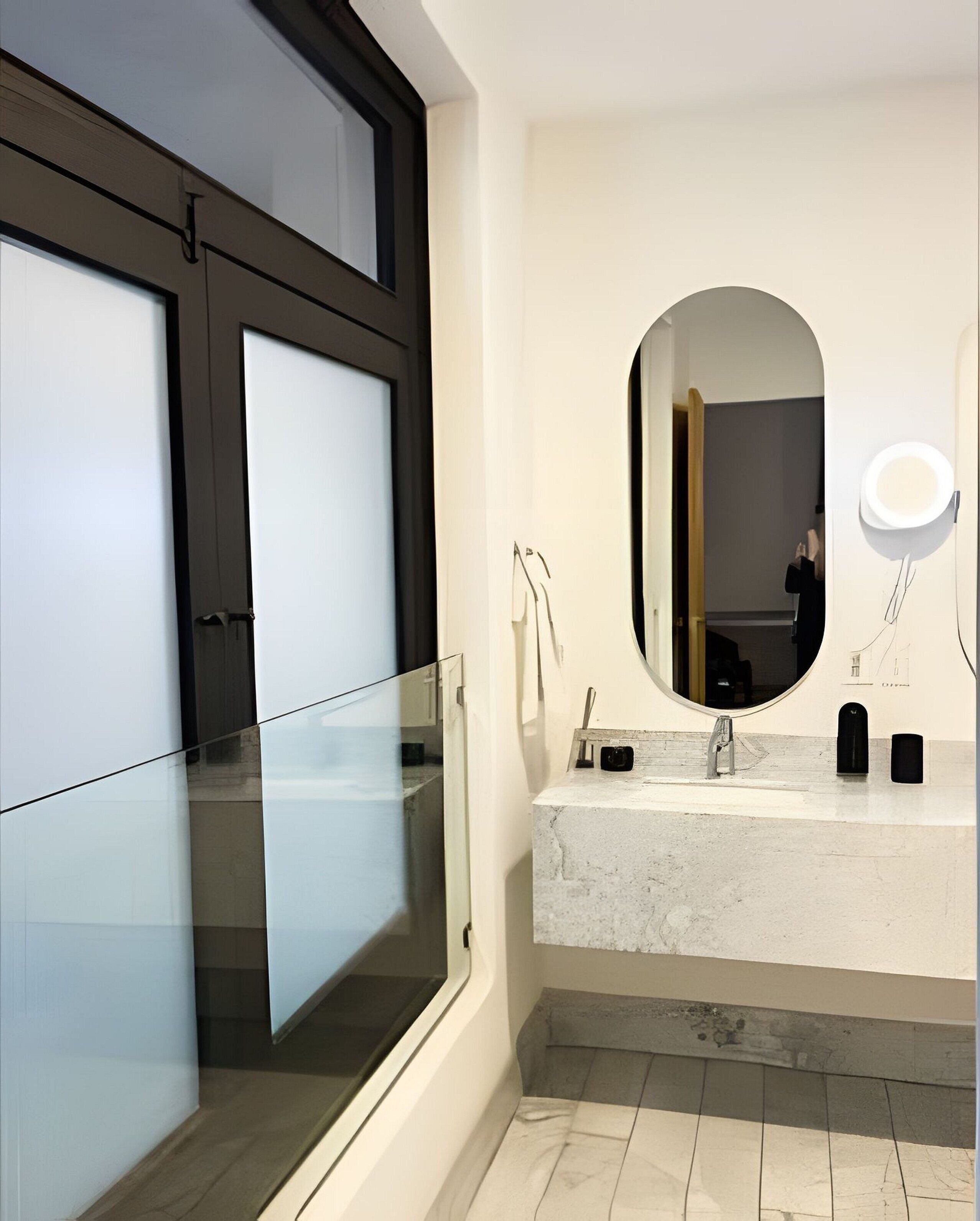 A modern bathroom with a glass shower enclosure, a marble sink, and a large mirror with a round mirror above it.
