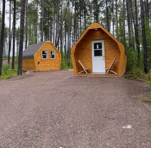 Two wooden cabins with a gravel driveway, surrounded by tall trees.