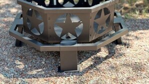 A hexagonal outdoor grill with a star design on the sides, set on a gravel surface.