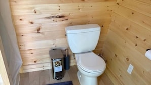 Une petite salle de bain aux murs lambrissés, équipée de toilettes, d’une poubelle et d’un tapis bleu sur le sol.