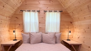 Une chambre confortable dans un chalet en bois, avec un grand lit, deux tables de chevet et deux fenêtres avec des rideaux.