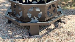 Un barbecue extérieur de forme hexagonale, orné d’un motif en étoile sur les côtés, posé sur une surface de gravier.