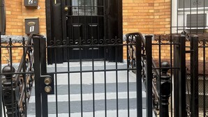 Une grille en métal noir mène à un bâtiment en briques dont les portes sont numérotées.