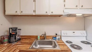 Una cocina con armarios blancos, un lavamanos de acero inoxidable, una cafetera y una estufa blanca.