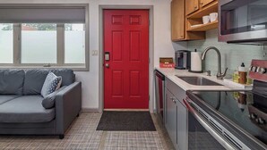 Una cocina compacta con una puerta roja, un sofá gris y un microondas.