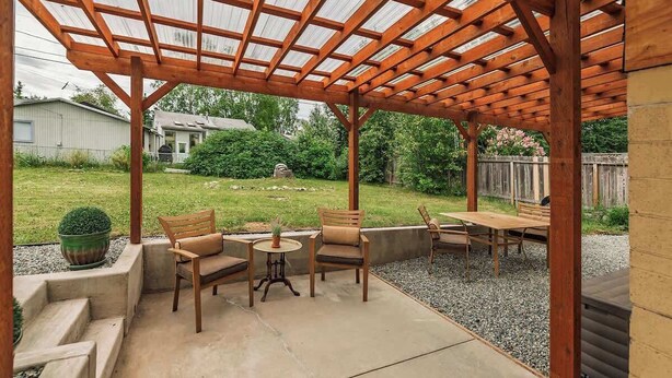 Un patio cubierto con un pérgola, mobiliario exterior y vista a un jardín trasero.