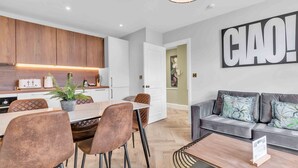 A modern kitchen with wooden cabinets, a dining area with brown chairs, and a living area with a grey sofa. - Hove Alone 5 Top Floor By My Getaways (Hove)