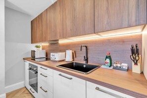 A modern kitchen with wooden cabinets, a stainless steel sink, a built-in oven, and a countertop with a toaster and a kettle. - Hove Alone 5 Top Floor By My Getaways (Hove)