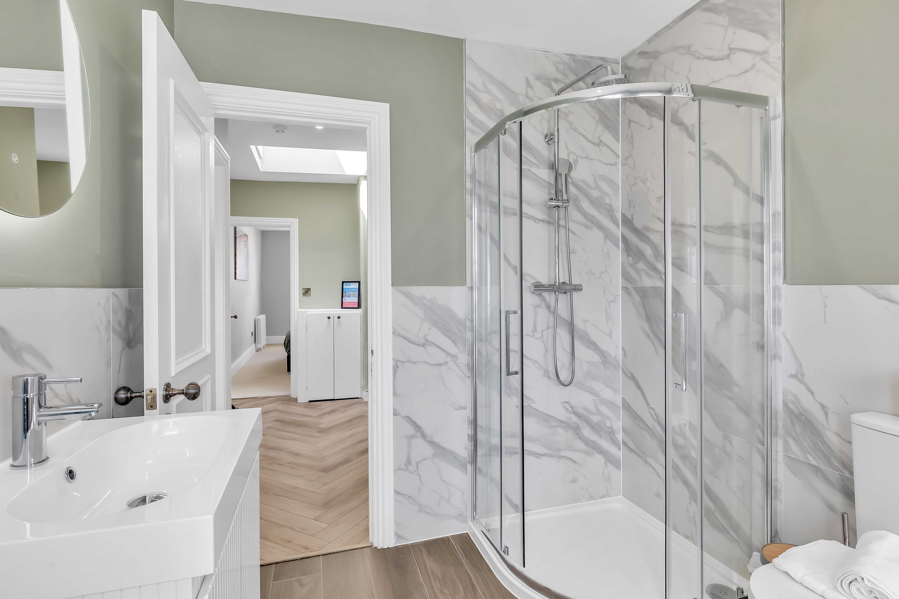 A modern bathroom with a glass-enclosed shower, a large mirror, and a white sink.