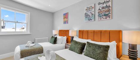 A hotel room with two beds, a window with a city view, and artwork on the wall.