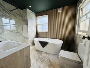 Een moderne badkamer met een vrijstaand bad, toilet en wastafel.