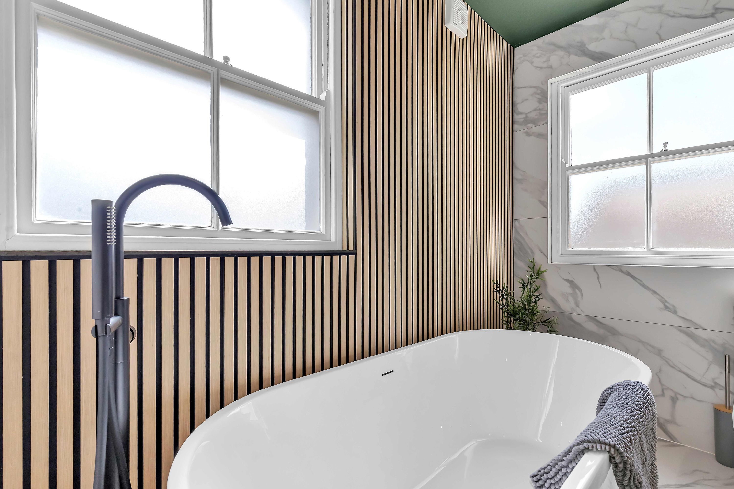 A modern bathroom with a freestanding bathtub, a towel rack, and a window with frosted glass.