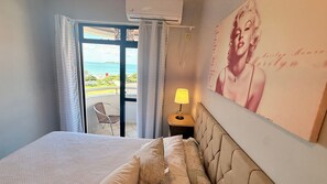 A hotel room with a bed, a lamp, a poster, and a view of the sea through a glass door. - Aguas de Marco  (Florianopolis)