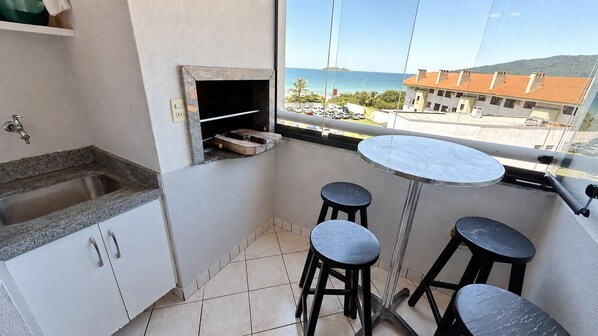 Uma cozinha compacta com pia, bancada e janela com vista para a rua e edifícios. Há dois bancos e uma pequena mesa.