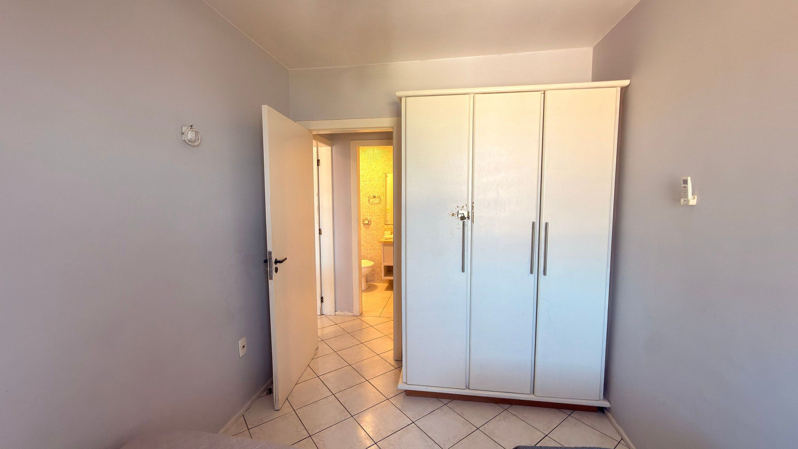 Un pasillo con un armario blanco, piso de baldosas y una puerta que da al baño.