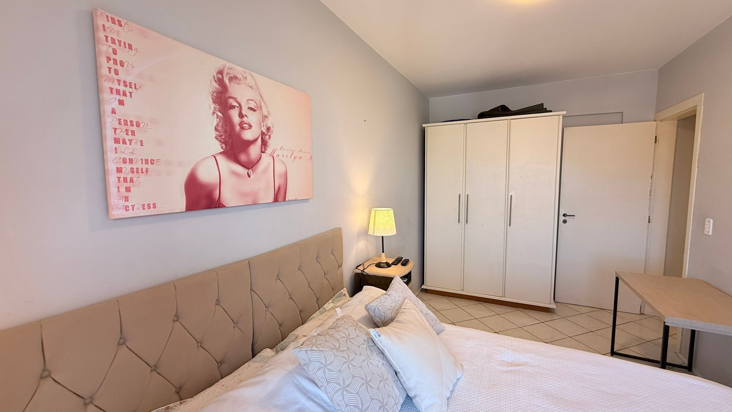 A bedroom with a bed, a nightstand, a lamp, a wardrobe, and a poster on the wall.