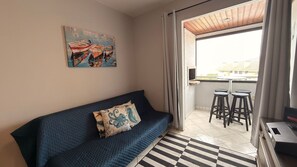 A room with a blue sofa, a painting of boats, a balcony with stools, and a checkered floor. - Aguas de Marco  (Florianopolis)