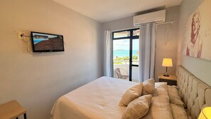 A bedroom with a bed, a TV mounted on the wall, a window with curtains, and an air conditioning unit. - Aguas de Marco  (Florianopolis)