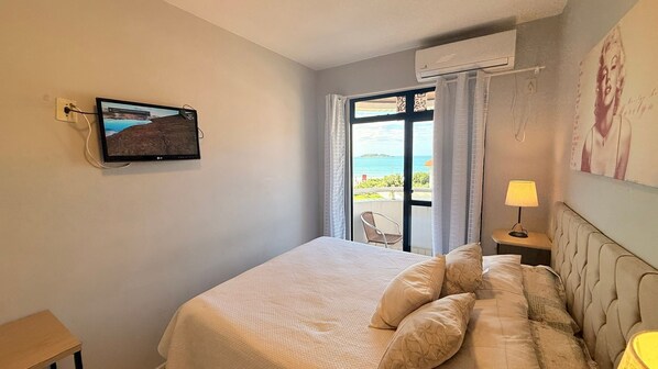A bedroom with a bed, a TV mounted on the wall, a window with curtains, and an air conditioning unit. - Aguas de Marco  (Florianopolis)