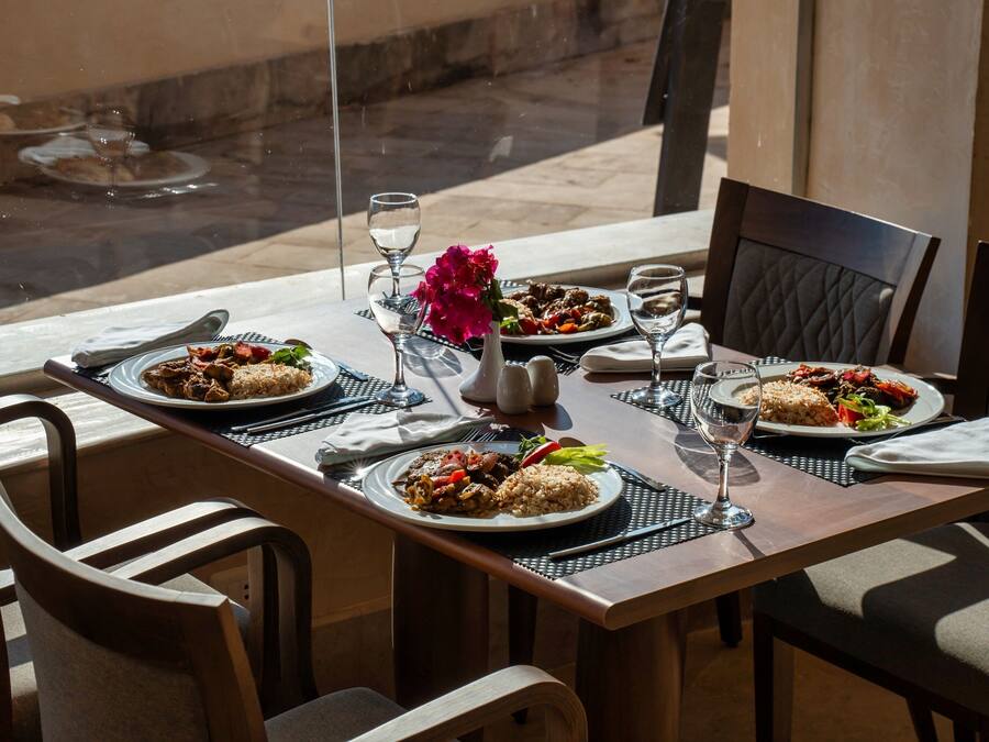 Una mesa de comedor dispuesta con platos de comida, vasos y un centro de mesa con flores.
