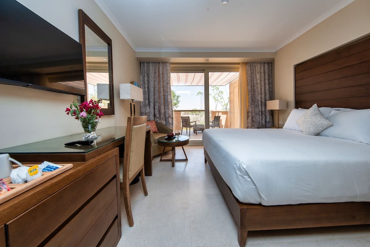 Una camera d'albergo con un letto, una scrivania, una sedia, un tavolino e una grande finestra.