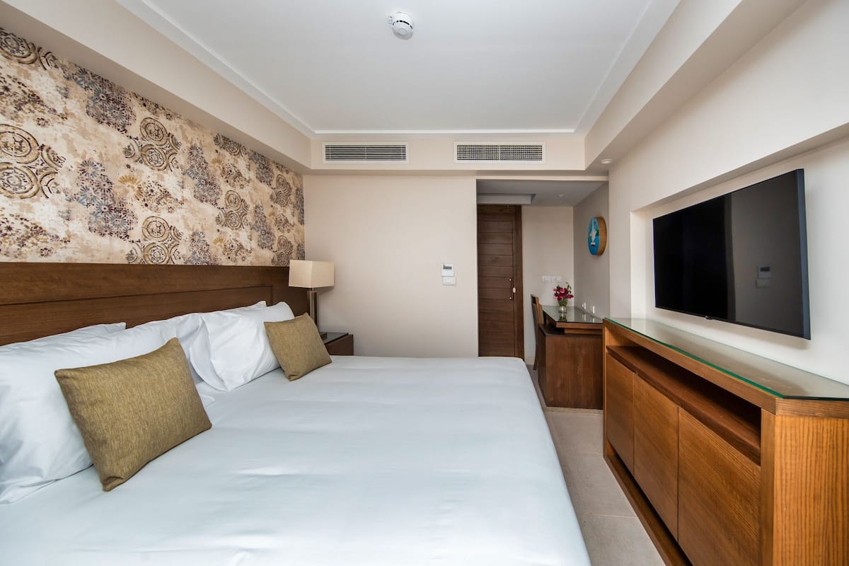 Una camera d'albergo con un letto grande, una testiera in legno, una TV fissata al muro e un comò in legno.